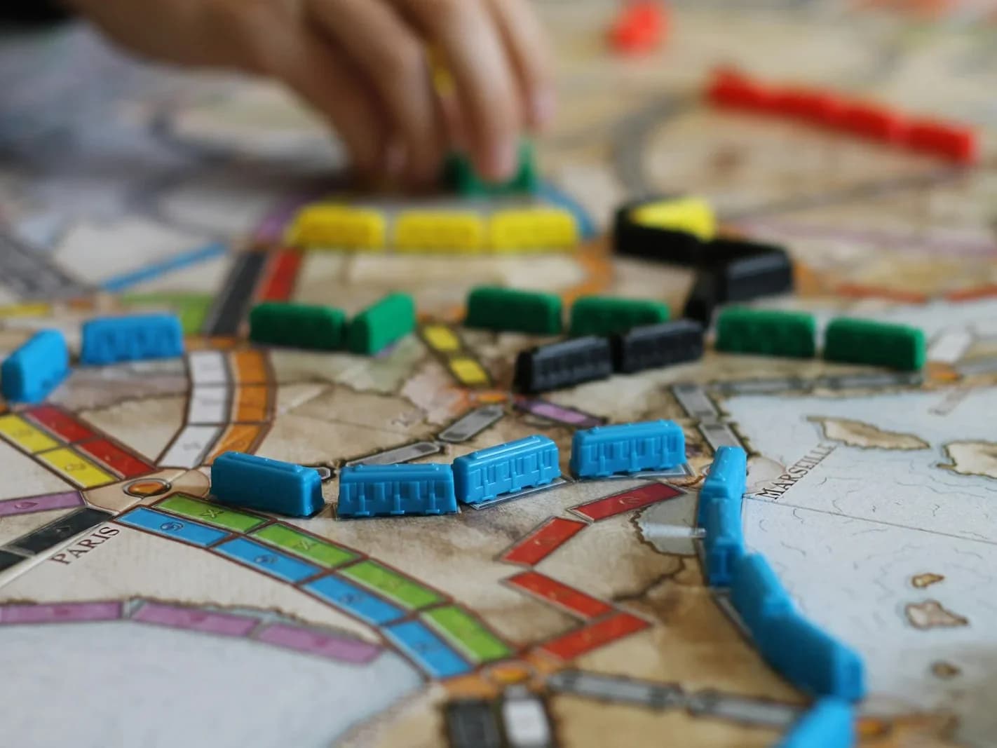 Hände bewegen eine Spielfigur auf einem Brettspiel mit Karten und Marken am Holztisch