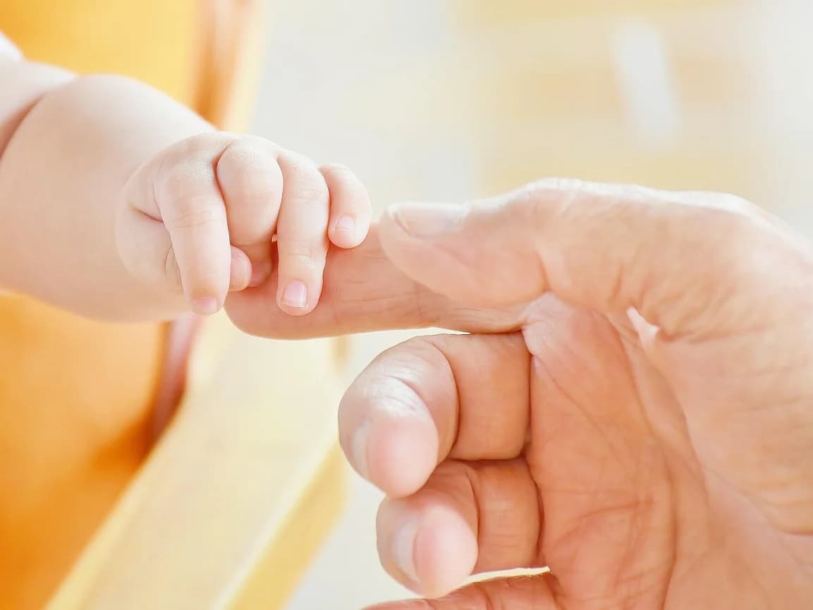 Eine Babyhand umfasst den Finger eines Erwachsenen.