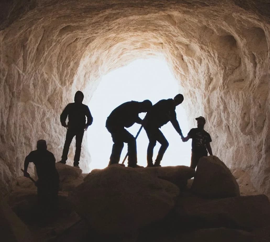 Ein Eingang zu einer Höhle mit einer Gruppe an Entdeckern im Gegenlicht fotografiert. Stellvertretend für die Höhlenforschung Oberpfalz