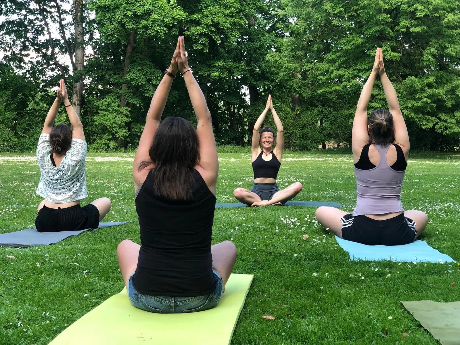 Frauen sitzen im Park auf Gymnastikmatten und machen Yogaübungen.