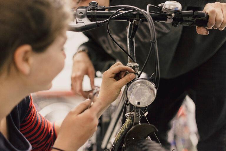 Eine Frau befestigt eine Lampe am Fahrrad in der Fahrradwerkstatt des Campus Asyl.