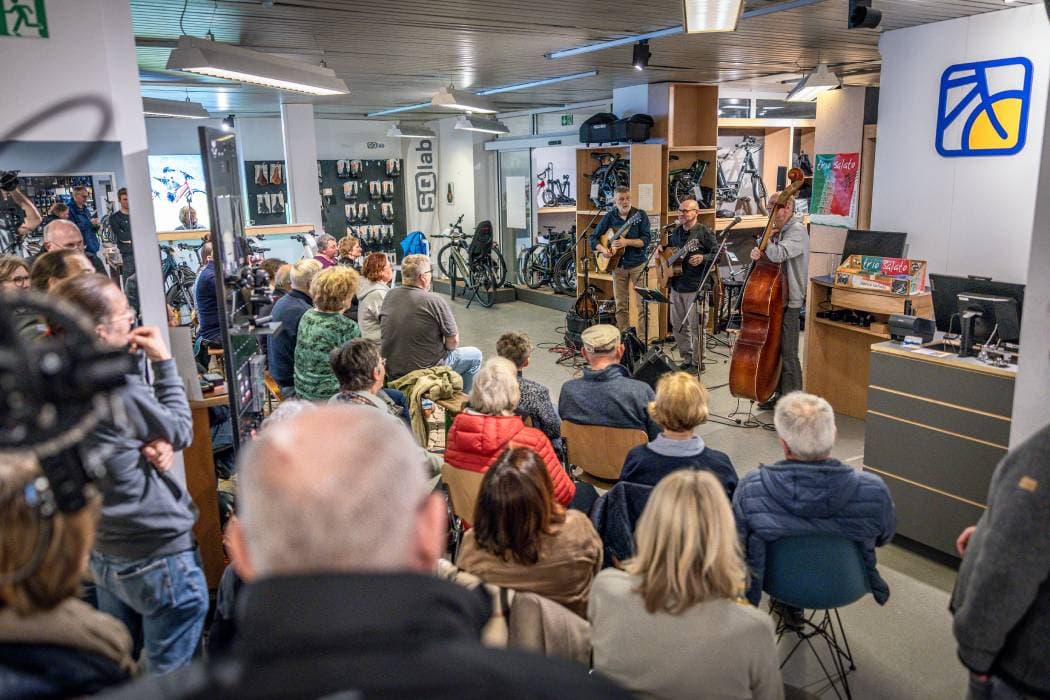 Viele Zuhörer sitzen in einem Radladen bei einem Konzert.