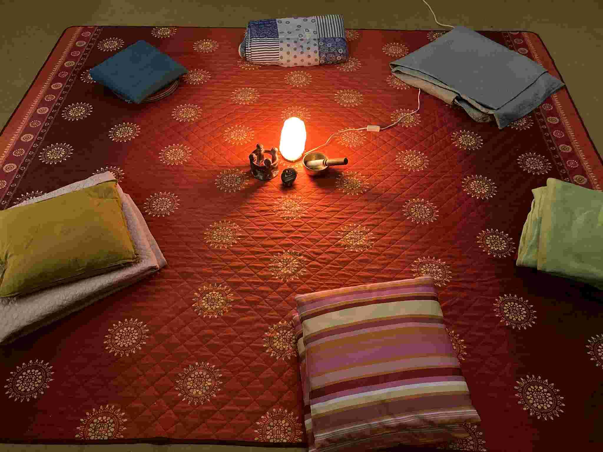 Sitzkissen liegen im Kreis auf einem Teppich um eine Mitte mit Kerze für die Meditationsgruppe