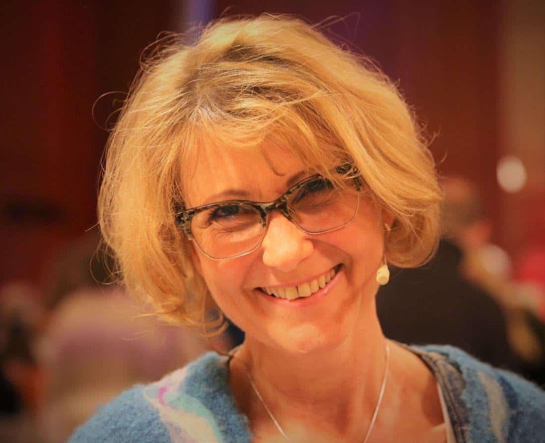 Nahaufnahme von Susanne Goebel mit Brille und einem Mikrofon. Sie lächelt und ist gerade bei den Chantabenden in Regensburg.