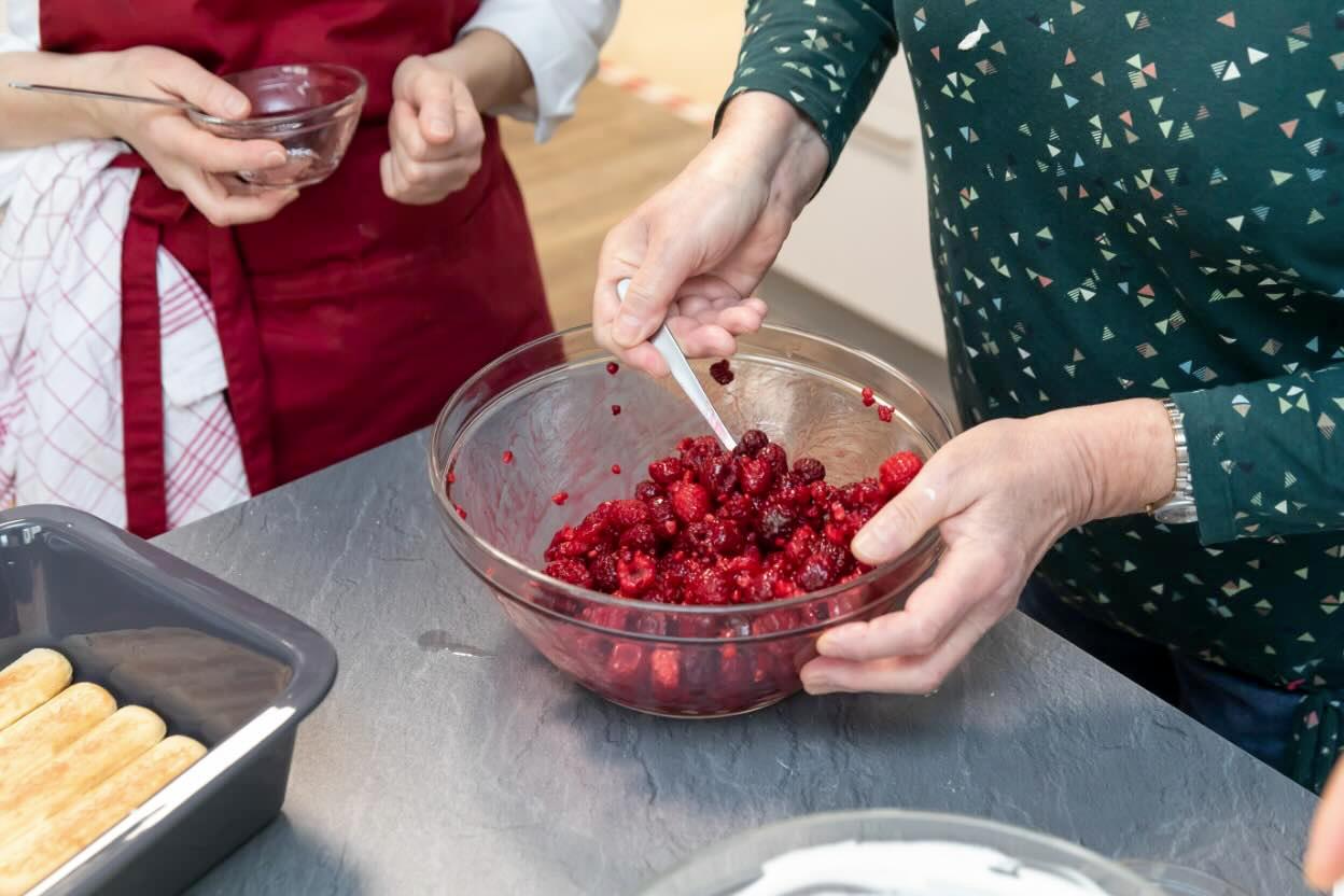 Senioren bereiten eine Nachspeise mit frischen Beeren zu.