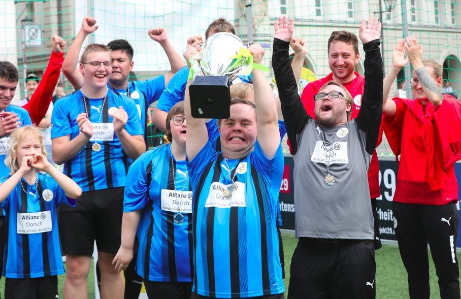 Menschen mit Handicap halten lachend einen Fußballpokal in die Höhe.