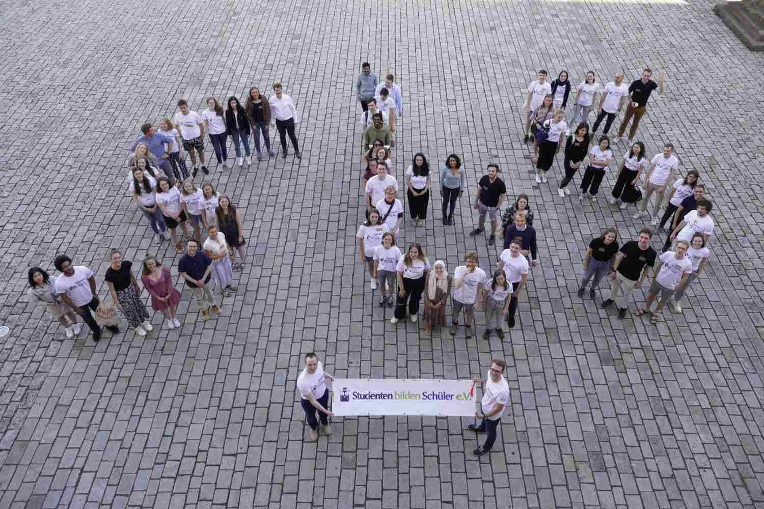 Junge Menschen stehen auf einem Platz und bilden die Buchstaben SbS.