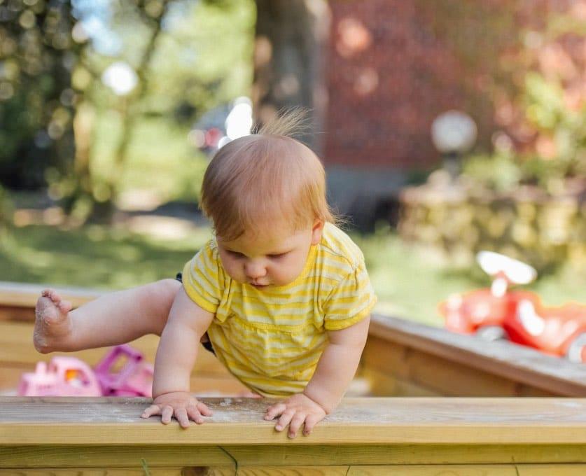Ein Baby, dass aus dem Sandkasten steigt stellvertretend für den Babyspielplatz Herztöne in Burgweinting, Regensburg.