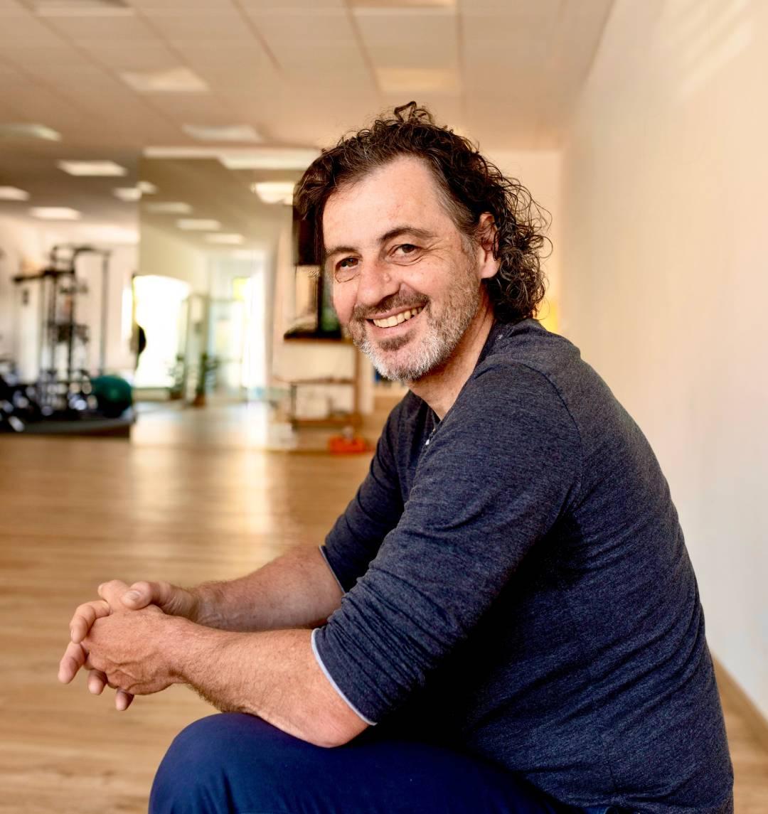 Der Feldenkraislehrer Bernhard sitzt entspannt im Trainingsraum und lächelt in die Kamera.