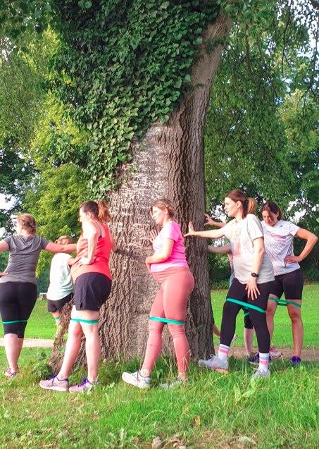 Frauen und Schwangere laufen im Park um einen Baum.