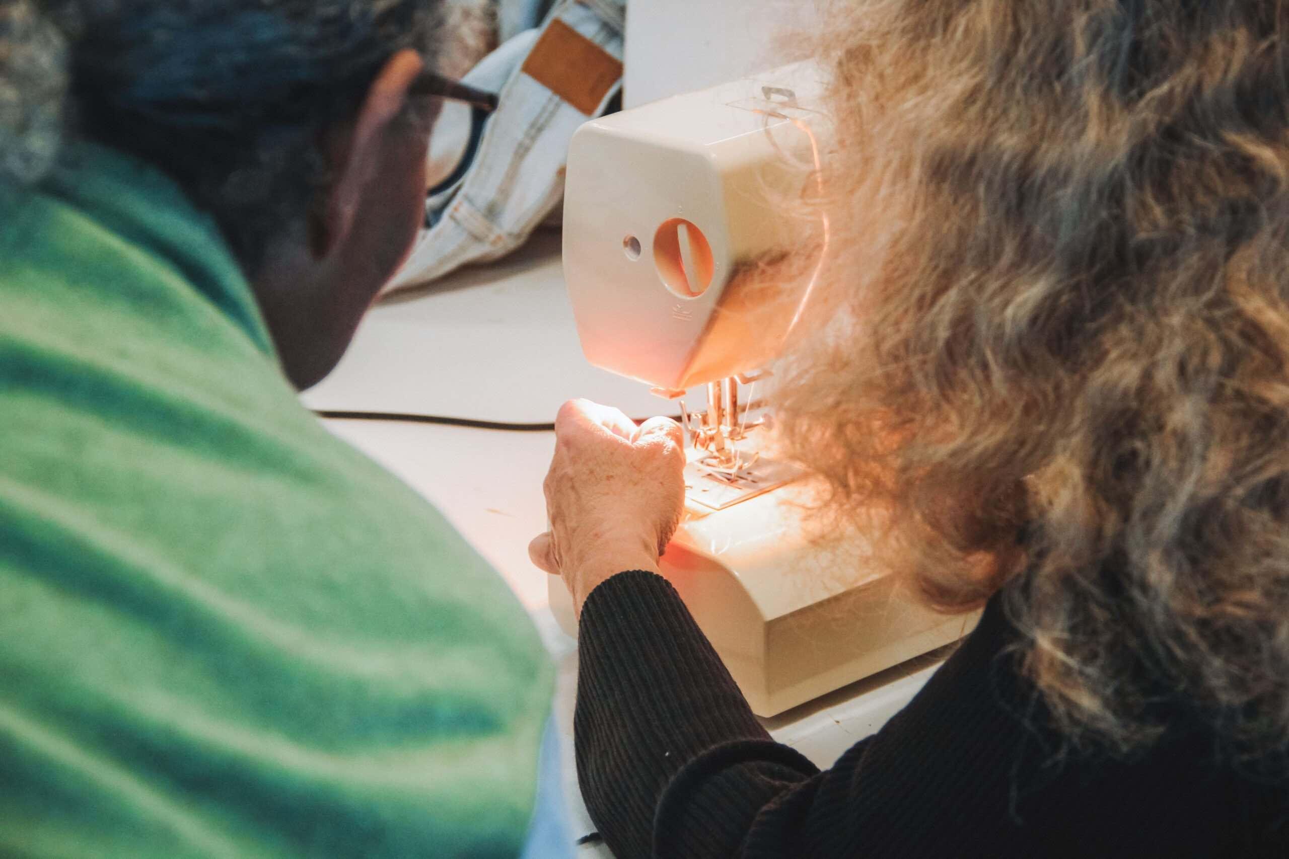 Eine Dame, welche bei der Nähwerkstatt von Campus Asyl an der Nähmaschine sitzt mit einem Herren.