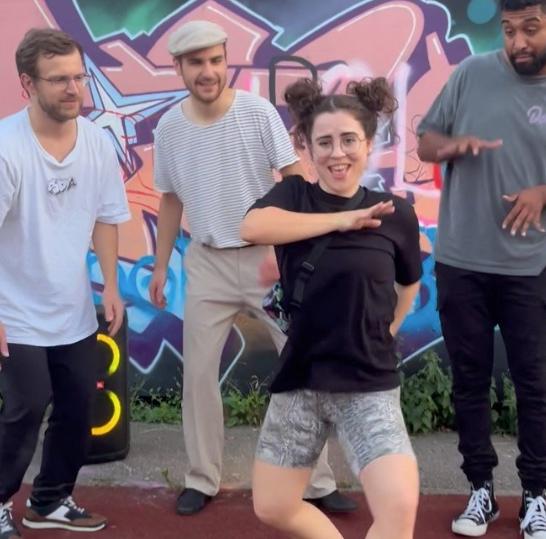 Regina Schweiger tanzt Dancehall in einem Kreis von Menschen hinter einem Graffiti in Regensburg.
