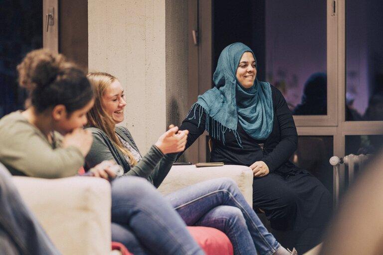 In einem einladenden Raum, dem Tower-Treff, teilen drei Menschen eine herzliche Atmosphäre, während sie gemeinsam lachen und das Zusammensein genießen.