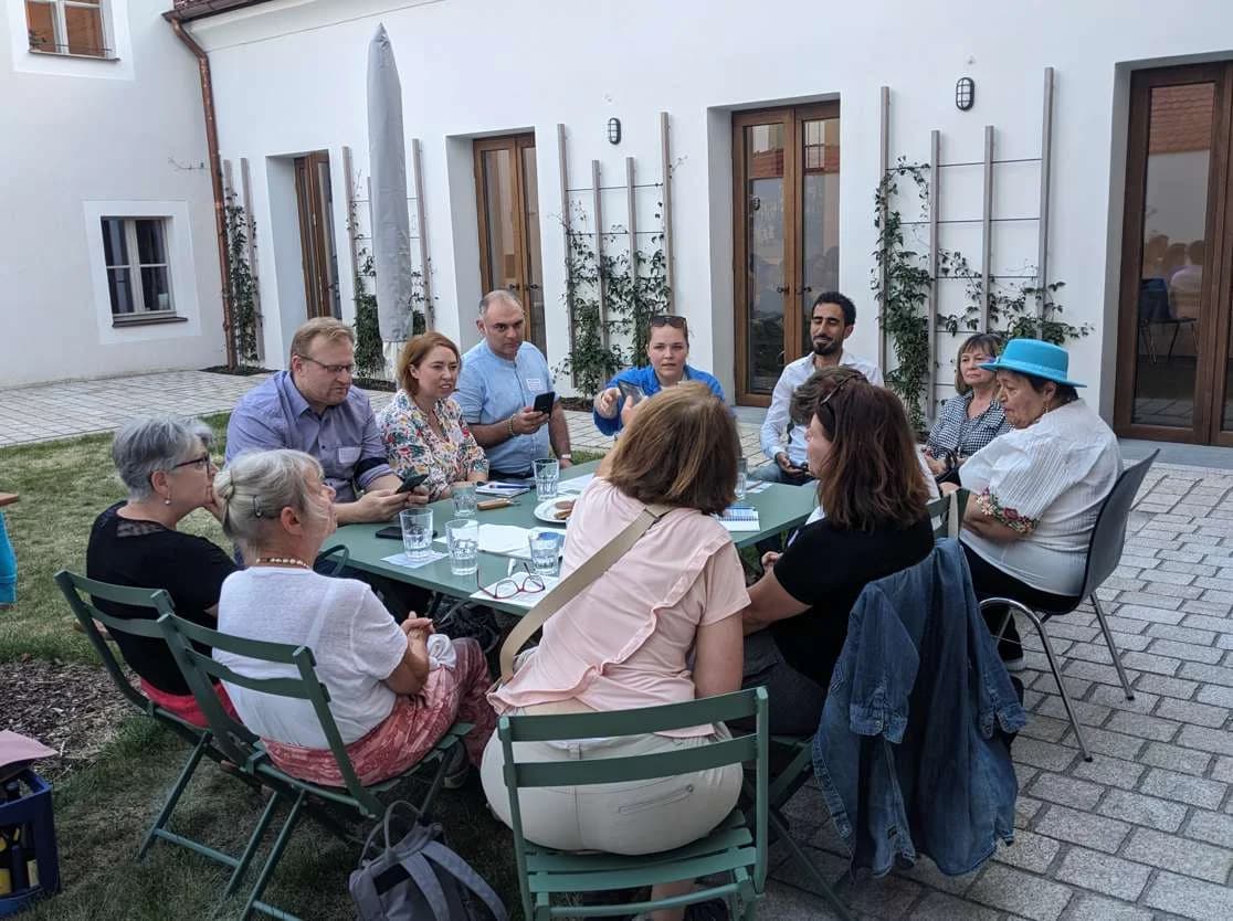 Menschen sitzen zusammen im Garten an einem Kaffeetisch.