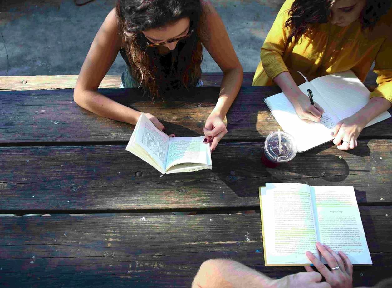 Menschen sitzen an einem Tisch mit Büchern bei einem Lesekreis und sprechen über die Bücher.