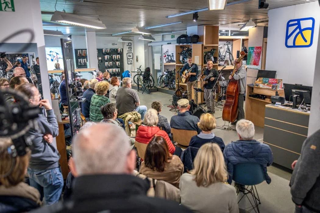 Viele Zuhörer sitzen in einem Radladen bei einem Konzert.