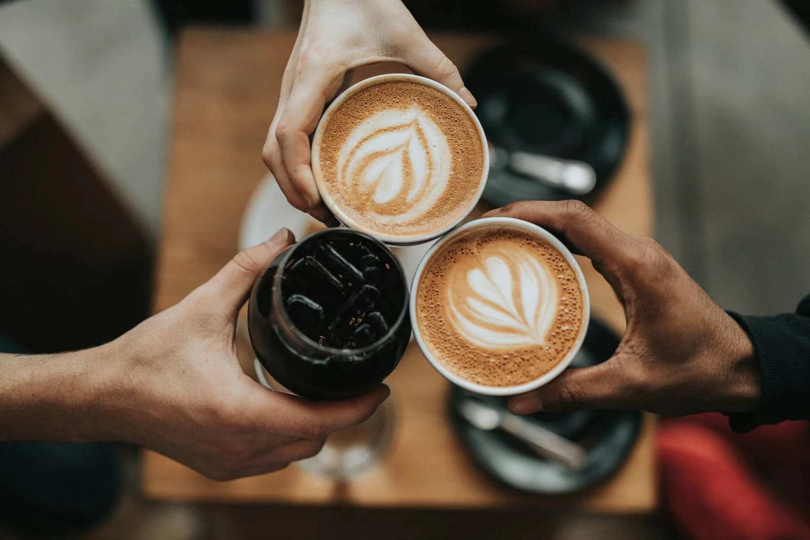 Drei Hände halten jeweils einen Kaffeebecher und stoßen damit an.