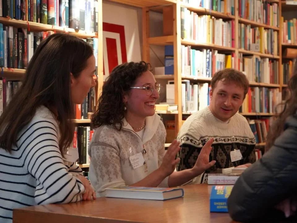Aufgeschlagenes Buch mit Stift und ein Notizheft auf einem Tisch vor einem Bücherregal
