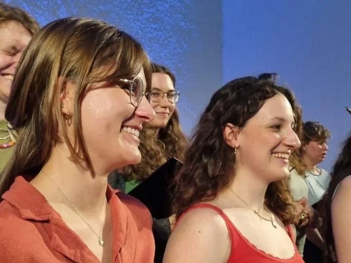 Aufgeschlagene Chornoten in roter Mappe, dahinter verschwommen weitere Chorsänger