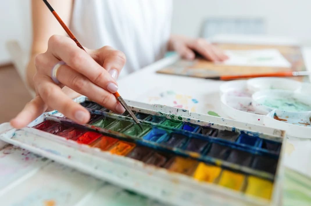 Ein Aquarellkasten wird mit dem Pinsel angerührt.