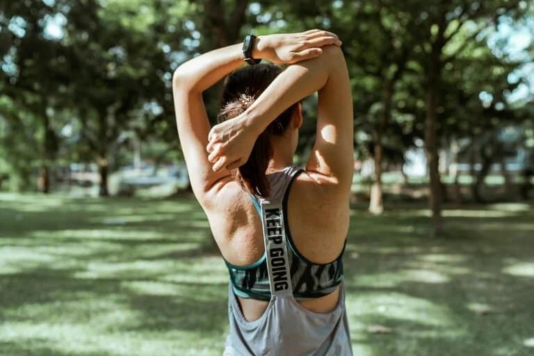 Eine Frau führt im Freien stehend Rückenübungen durch, stellvertretend für den Kurs "Sport im Park"