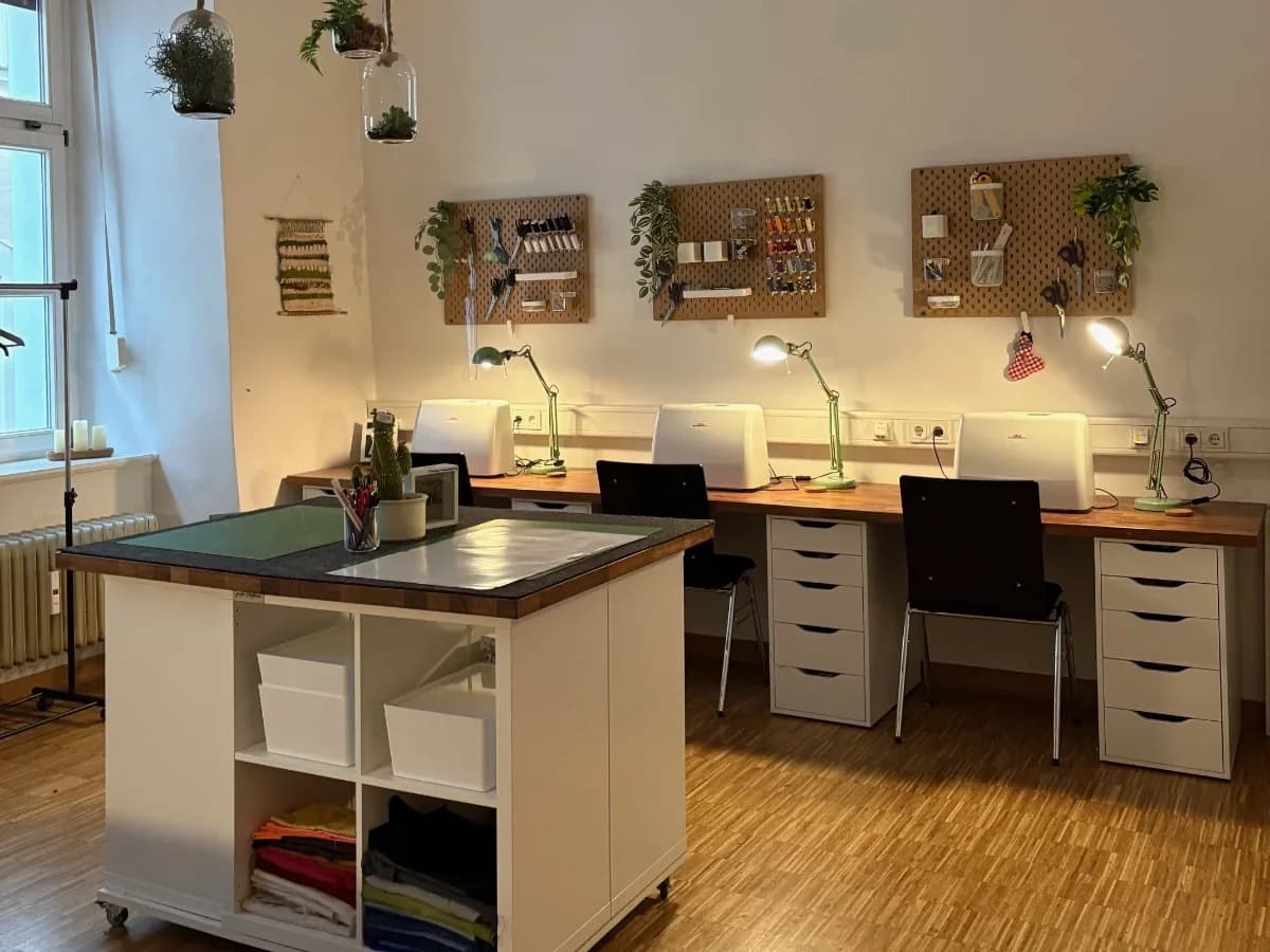 Heller Nähraum mit drei Nähmaschinen-Arbeitsplätzen, Werkzeugwänden und einem Zuschneidetisch im W1.