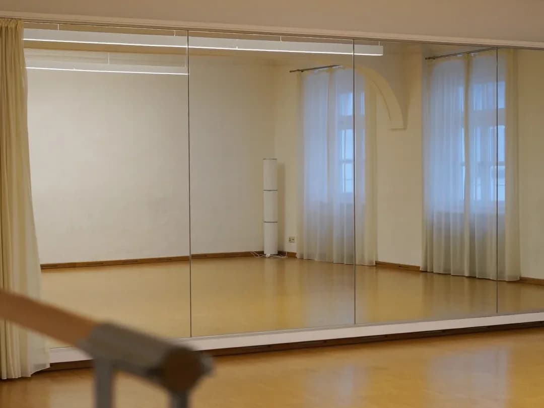 Leerer Tanzsaal mit Parkettboden, großer Spiegelwand und Ballettstange in einem Altbau