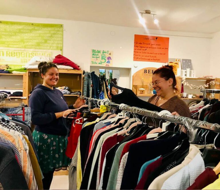 Zwei Helferinnen der Teilbar bei Transition Regensburg, die lachend Second-Hand-Kleidung einsortieren