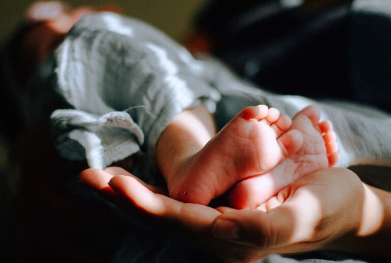 Beim Yoga mit Baby hält die Hand einer Mutter sanft, die Füße ihres Babys.