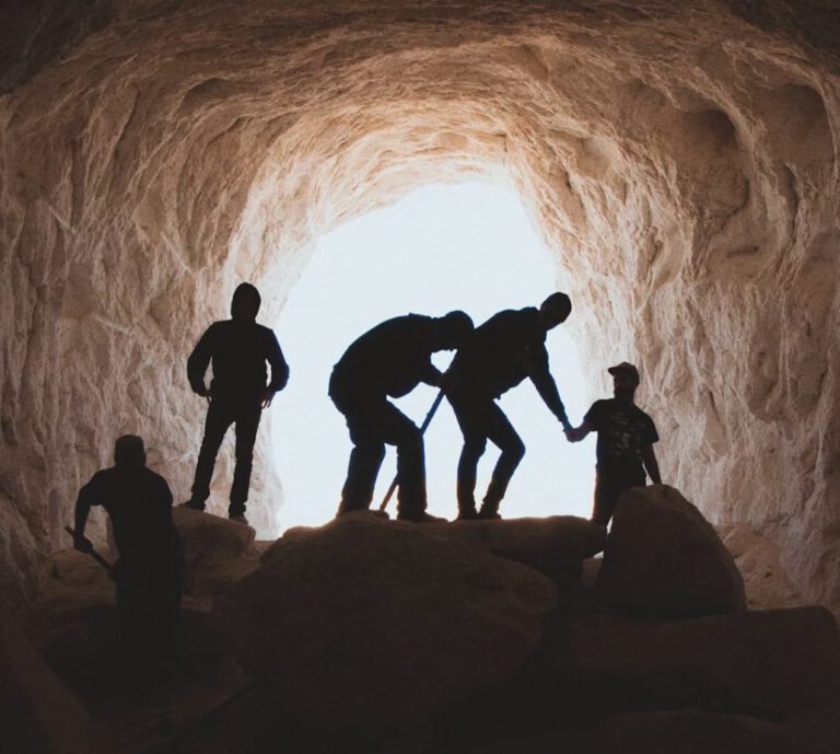 Ein Eingang zu einer Höhle mit einer Gruppe an Entdeckern im Gegenlicht fotografiert. Stellvertretend für die Höhlenforschung Oberpfalz