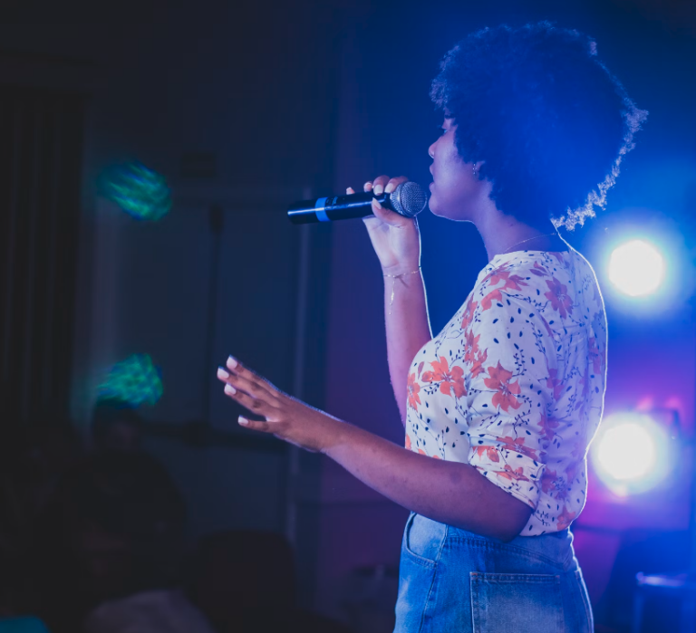 Eine junge Frau mit Afro, die vor Publikum singt, stellvertretend für das Karaoke im MGH
