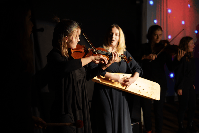 Eine Frau spielt eine Geige und Xenia Twarz die Veranstalterin von World Music Workshops, singt dazu.