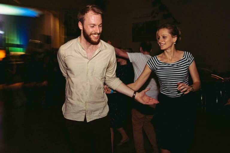 Ein junger Mann und eine junge Frau beim ausgelassenen Lindy-Hop Paartanz bei Swingmaniacs in Regensburg. Beide lachen.