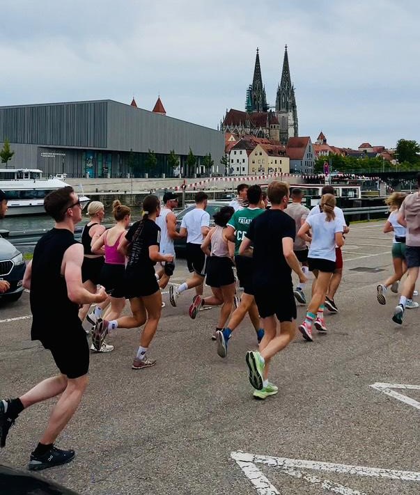 Eine Gruppe Läufer joggen mit Blick auf die Altstadt von Regensburg an der Donau entlang.