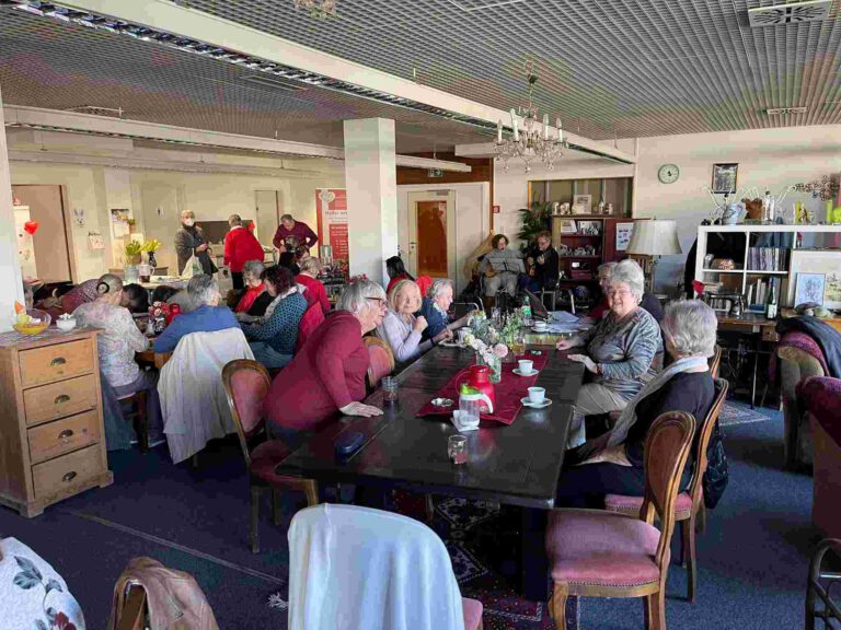 Eine große Gruppen Senioren sitzt bei Kaffee und Kuchen im Seniorencafe der Rengschburger Herzen, im Hintergrund spielt Musik.